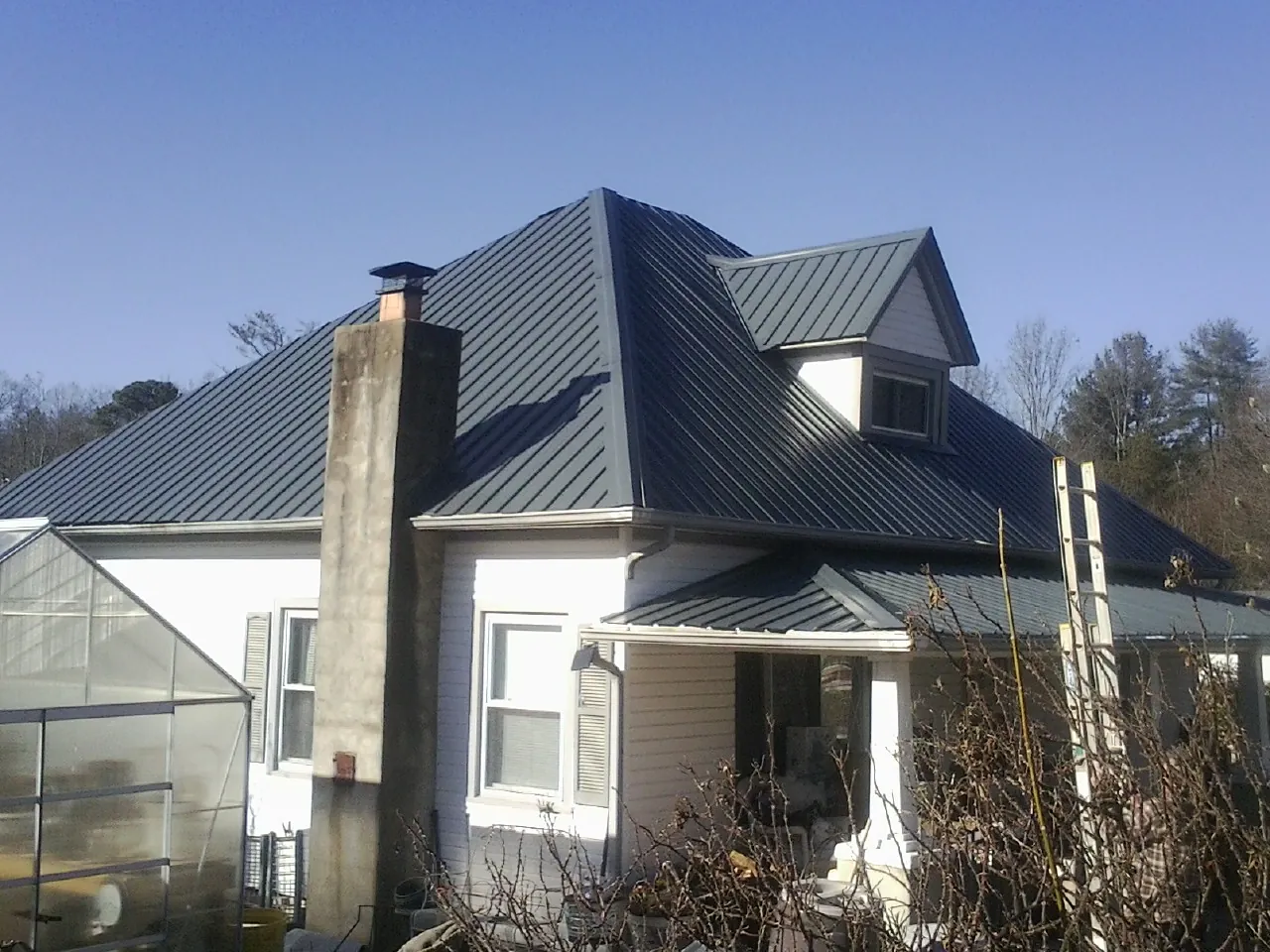 Dark blue standing seam metal roof on a white farmhouse with dormer — Slate & Tile Roof Repair by Roofing Brothers in Godley