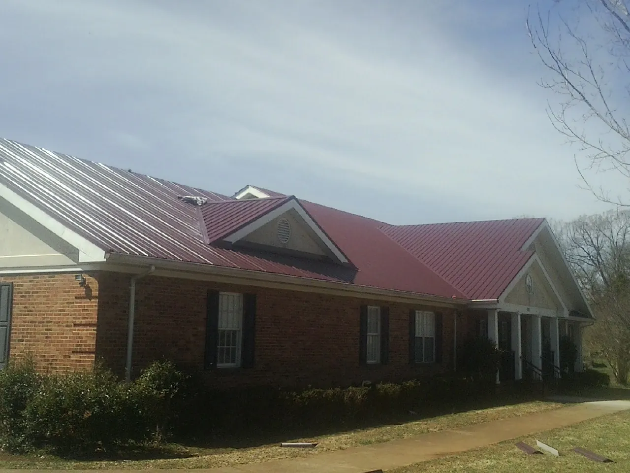 Red metal roof with gabled entries on a long brick building, from a Hail Damage Roof Repair job in Godley