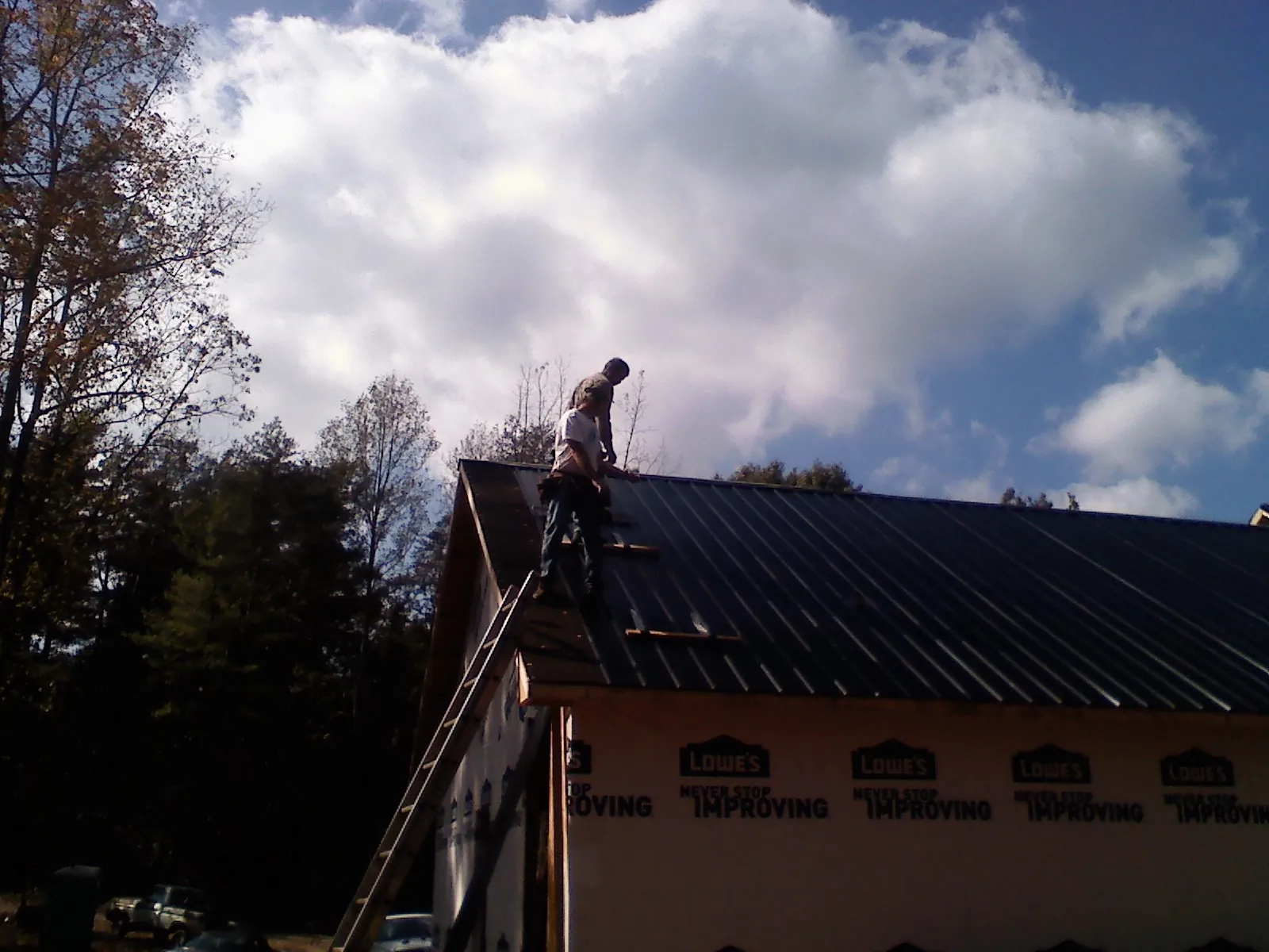 Roofer fastening dark metal panels high against a cloudy sky, from a Roof Inspection job in Godley