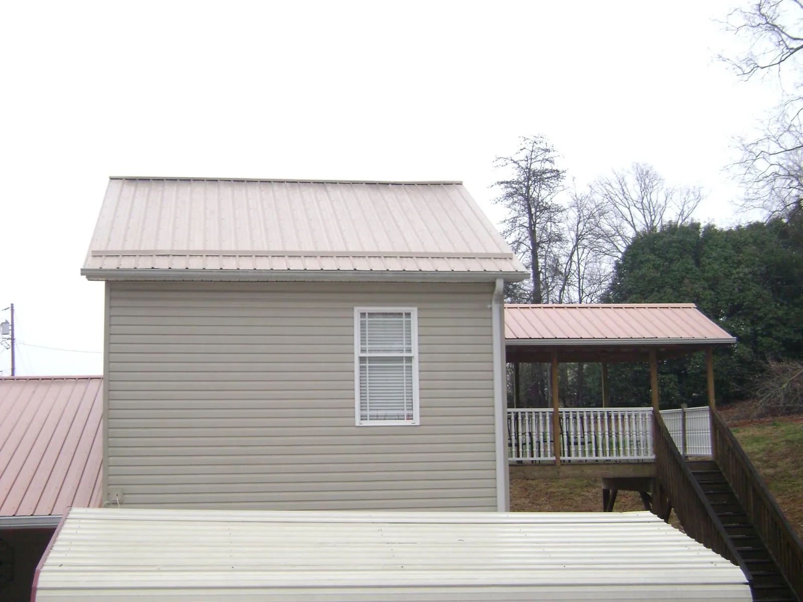 Tan metal roofs on a two story addition and attached porch, from a Roof Replacement job in Godley